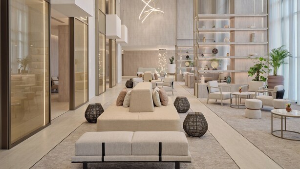 Een ruime lobby met een centraal zitgedeelte, een hoog plafond met moderne verlichting, en een groot raam dat natuurlijk licht binnenlaat.