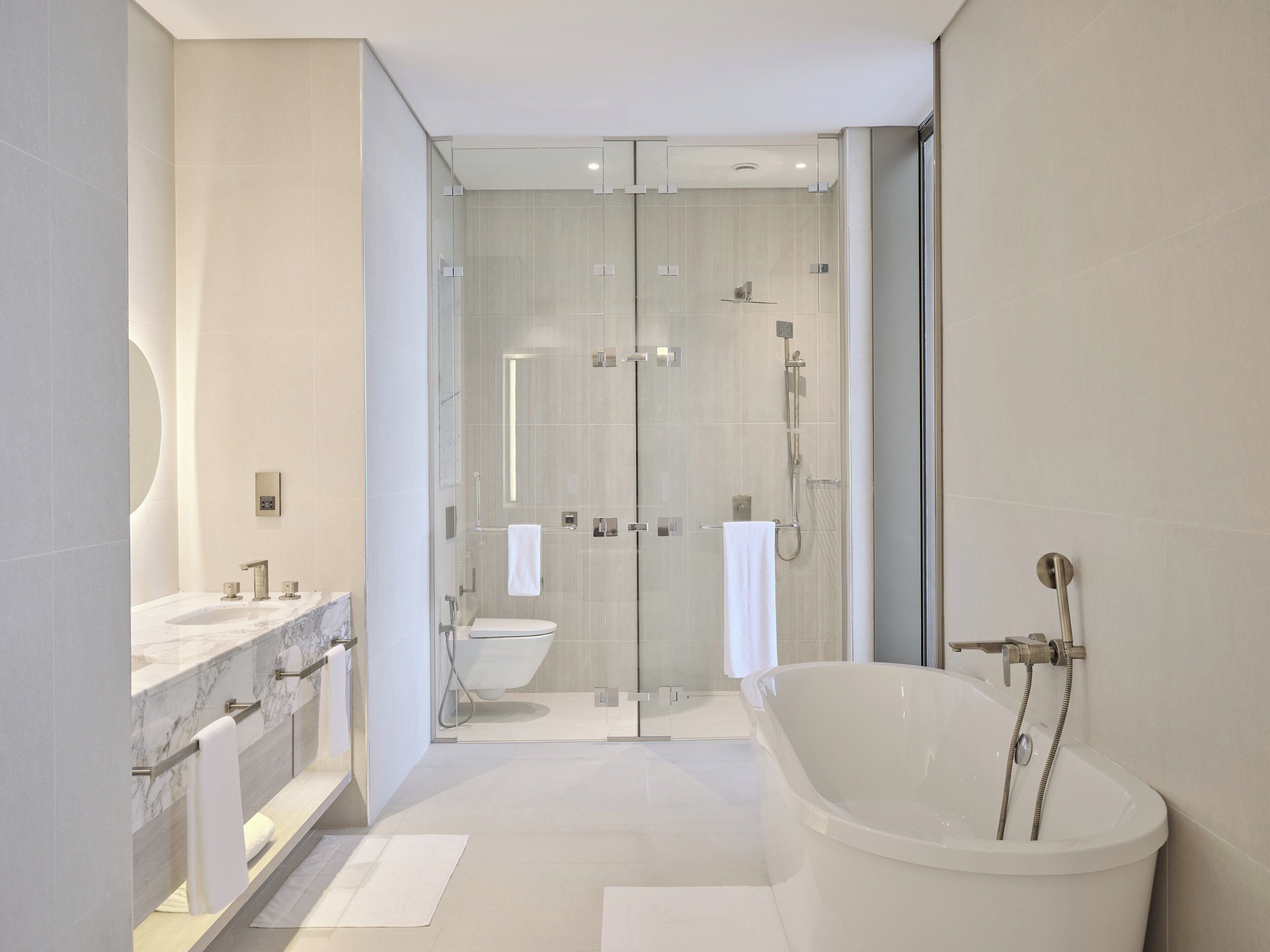 Un baño moderno con ducha de vidrio, una bañera independiente y un tocador con encimera de mármol.