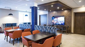 A modern dining area with orange chairs and dark tables, a large TV screen, and a wooden accent wall. - Holiday Inn Express and Suites Prince Albert South by IHG (Prince Albert)