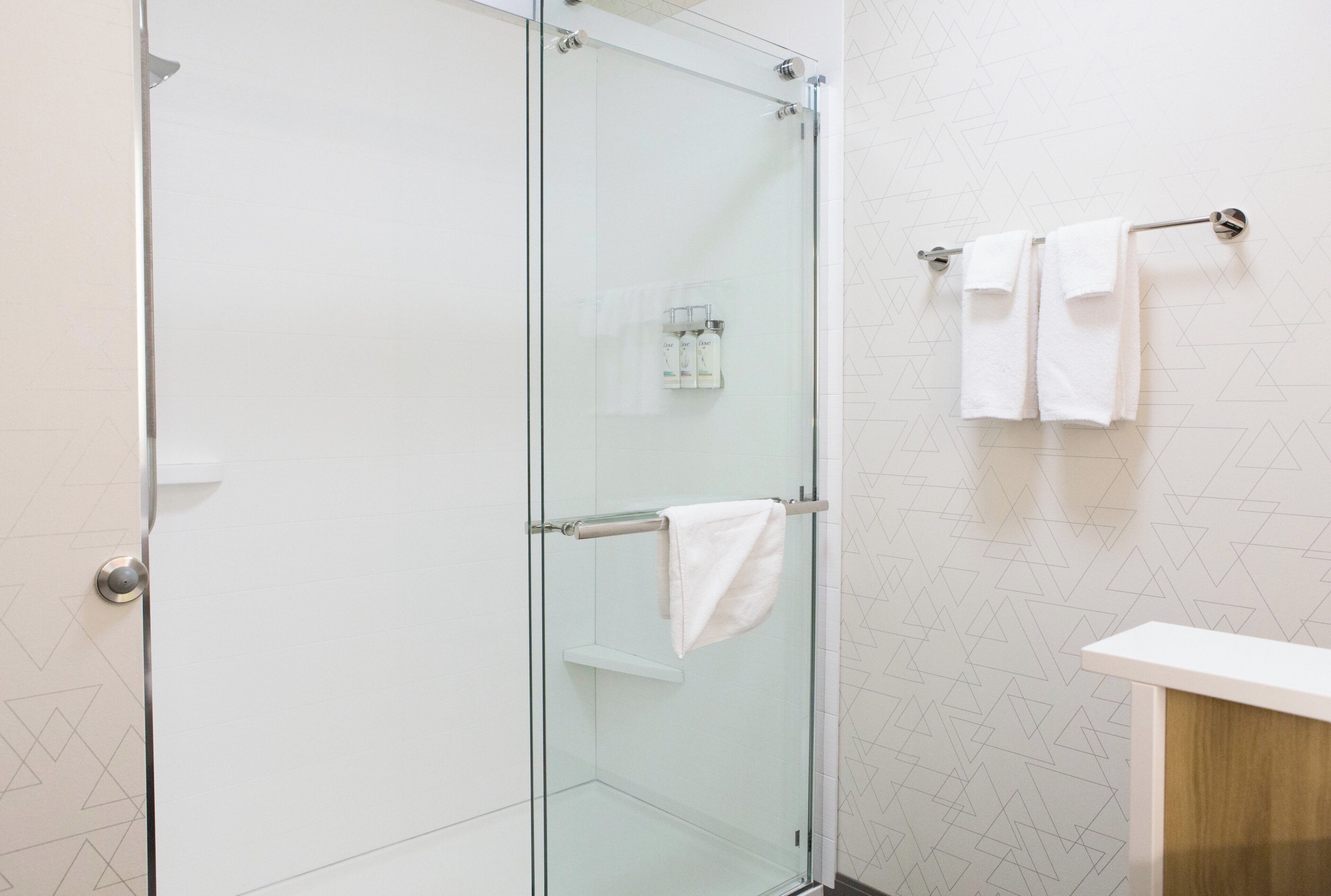 A modern bathroom with a glass shower enclosure, a white towel rack, and a geometric-patterned wall.