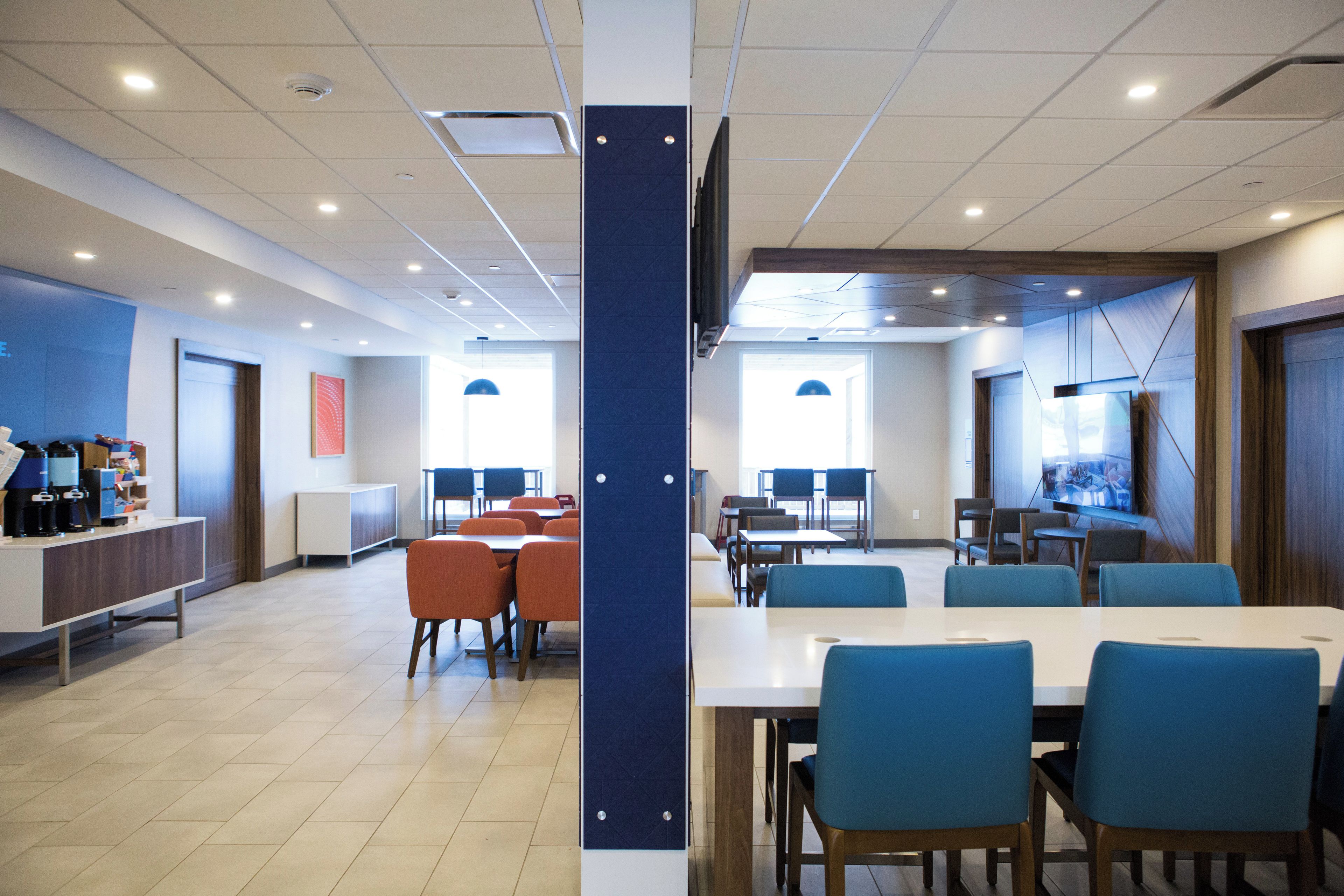 A modern conference room with tables and chairs, a coffee station, and a large screen.