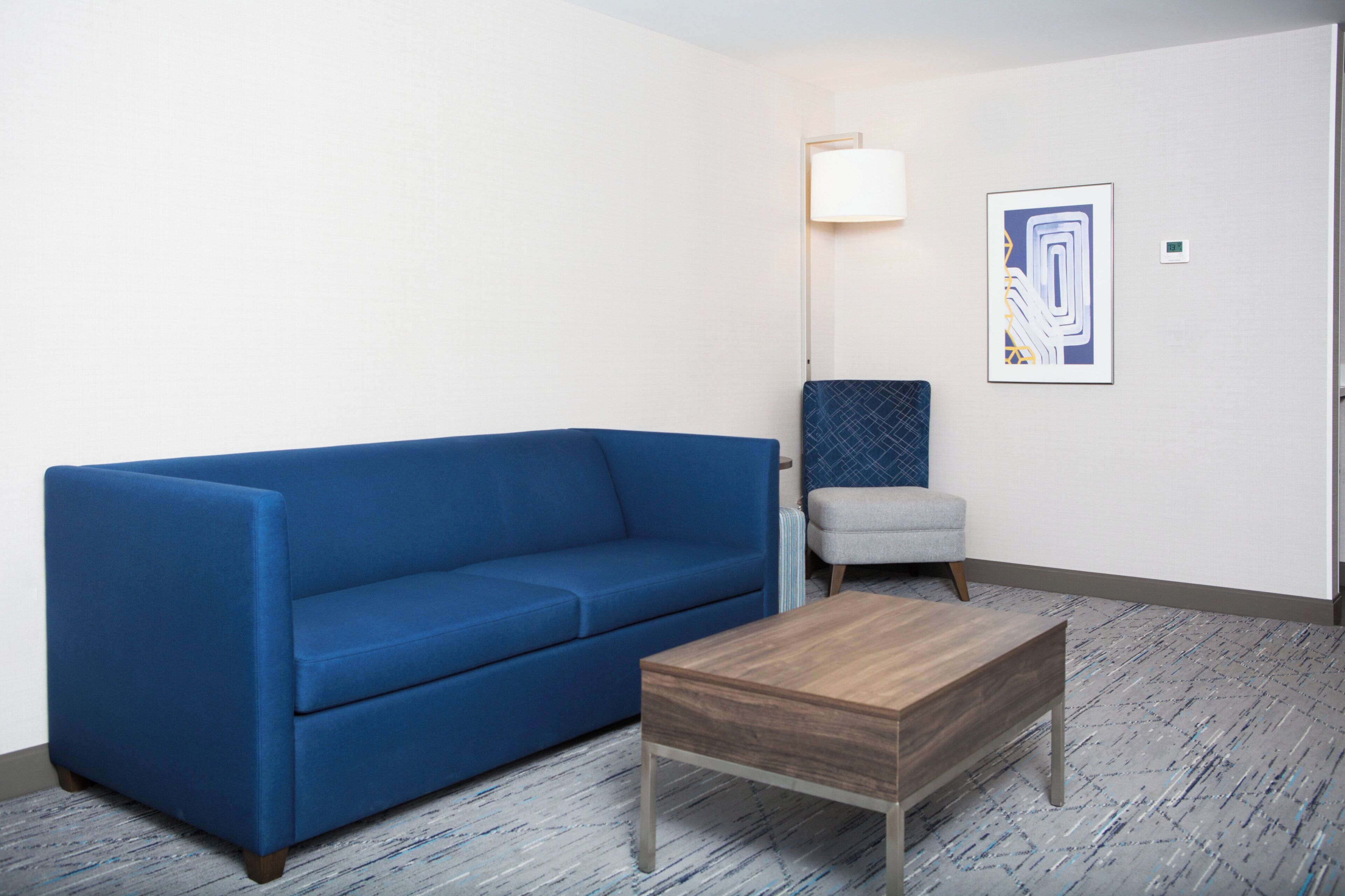 A room with a blue sofa, a wooden coffee table, a gray armchair, a floor lamp, and a framed abstract art piece on the wall.