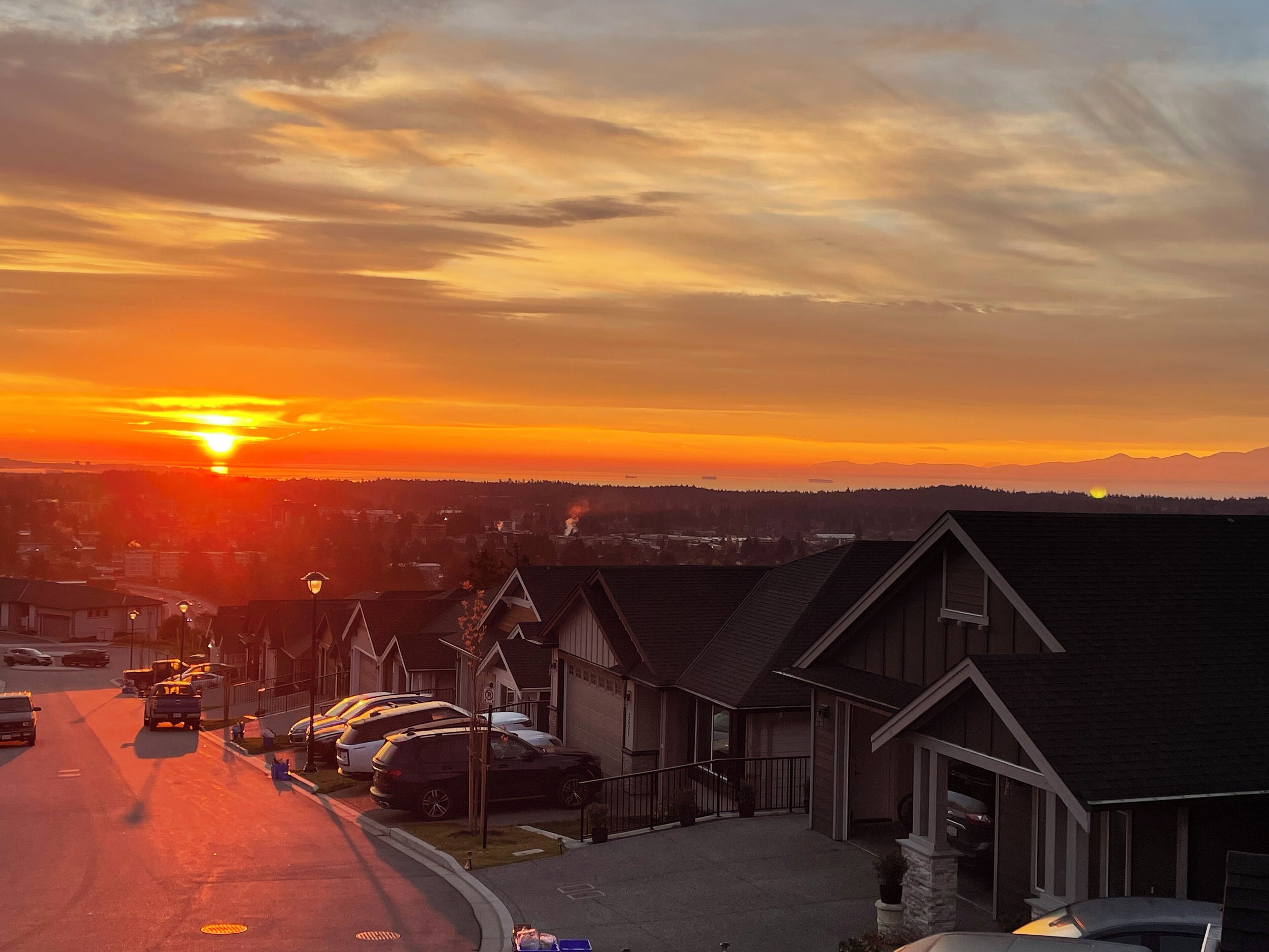 Een woonstraat in de zonsondergang, met huizen en geparkeerde auto's.