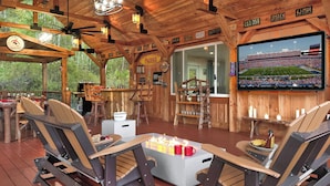 A rustic wooden deck with outdoor seating, a fire pit, and a mounted TV screen.