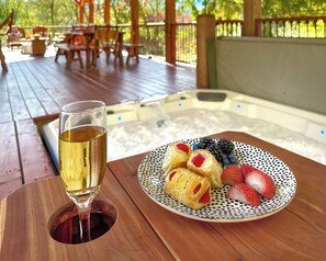 A wooden table with a glass of white wine, a plate with pastries and berries, and a hot tub in the background.