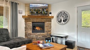 A living room with a stone fireplace, a flat-screen TV, and a decorative tree wall art piece.