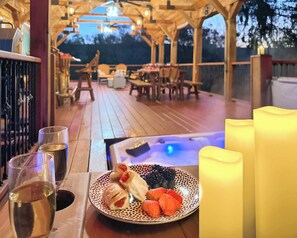 Una terraza de madera con un jacuzzi, una mesa de comedor con sillas, y un plato de pasteles y bayas.