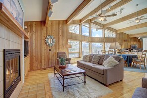 Ein geräumiges Wohnzimmer mit Kamin, Holzwänden, einem großen Fenster und einem Deckenventilator.