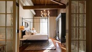A bedroom with a four-poster bed, a chandelier, and a large window with curtains.