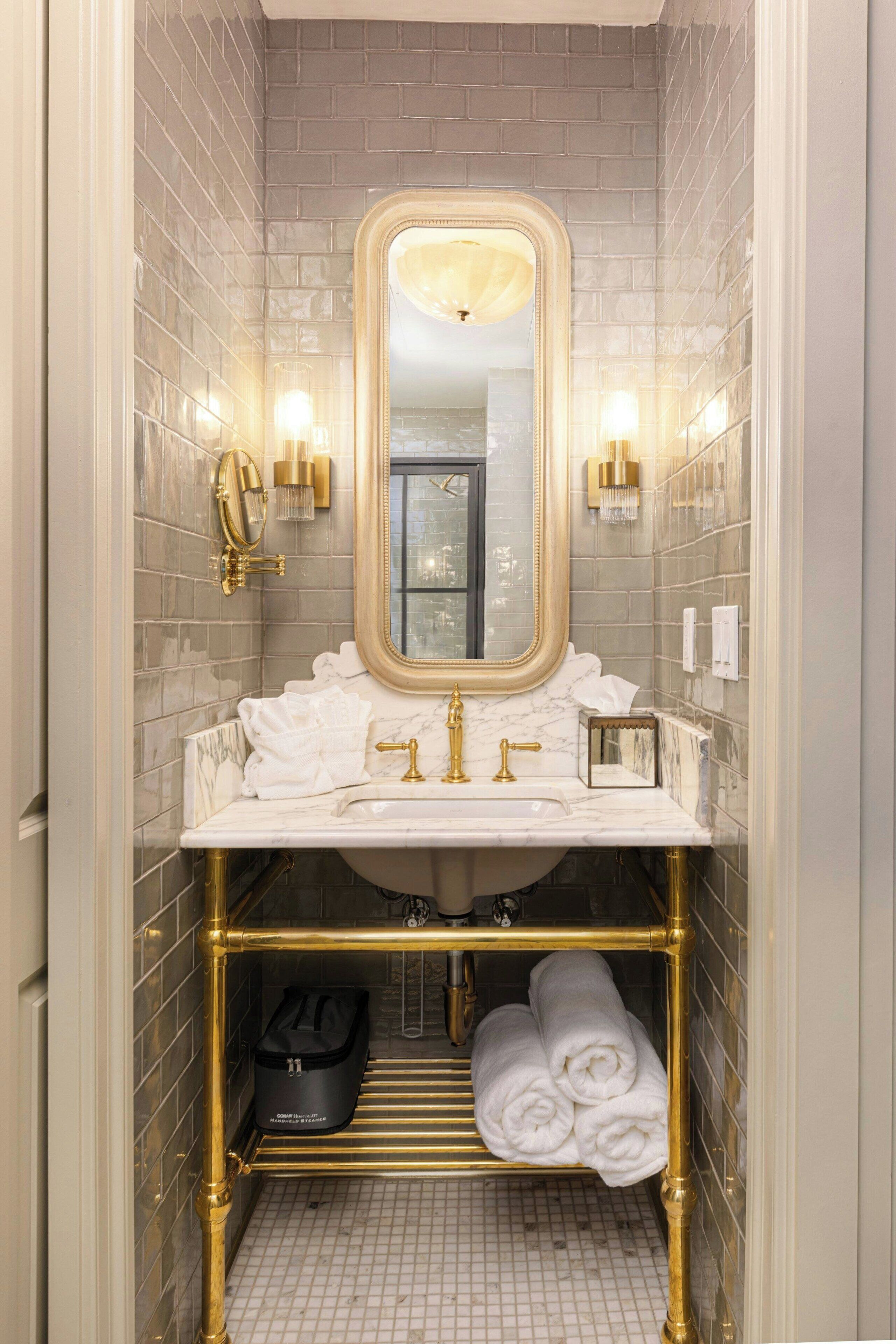 Une salle de bain dotée d’un lavabo en marbre, de robinetterie dorée, d’un grand miroir et d’un porte-serviettes avec des serviettes.
