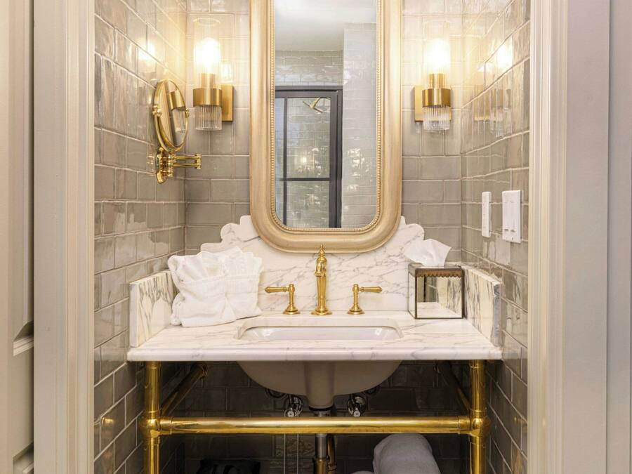 Un bagno con lavabo in marmo, accessori dorati, uno specchio grande e un porta asciugamani con asciugamani.