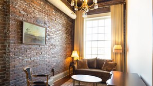 A cozy room with a brick wall, a wooden chair, a sofa, a coffee table, and a lamp.