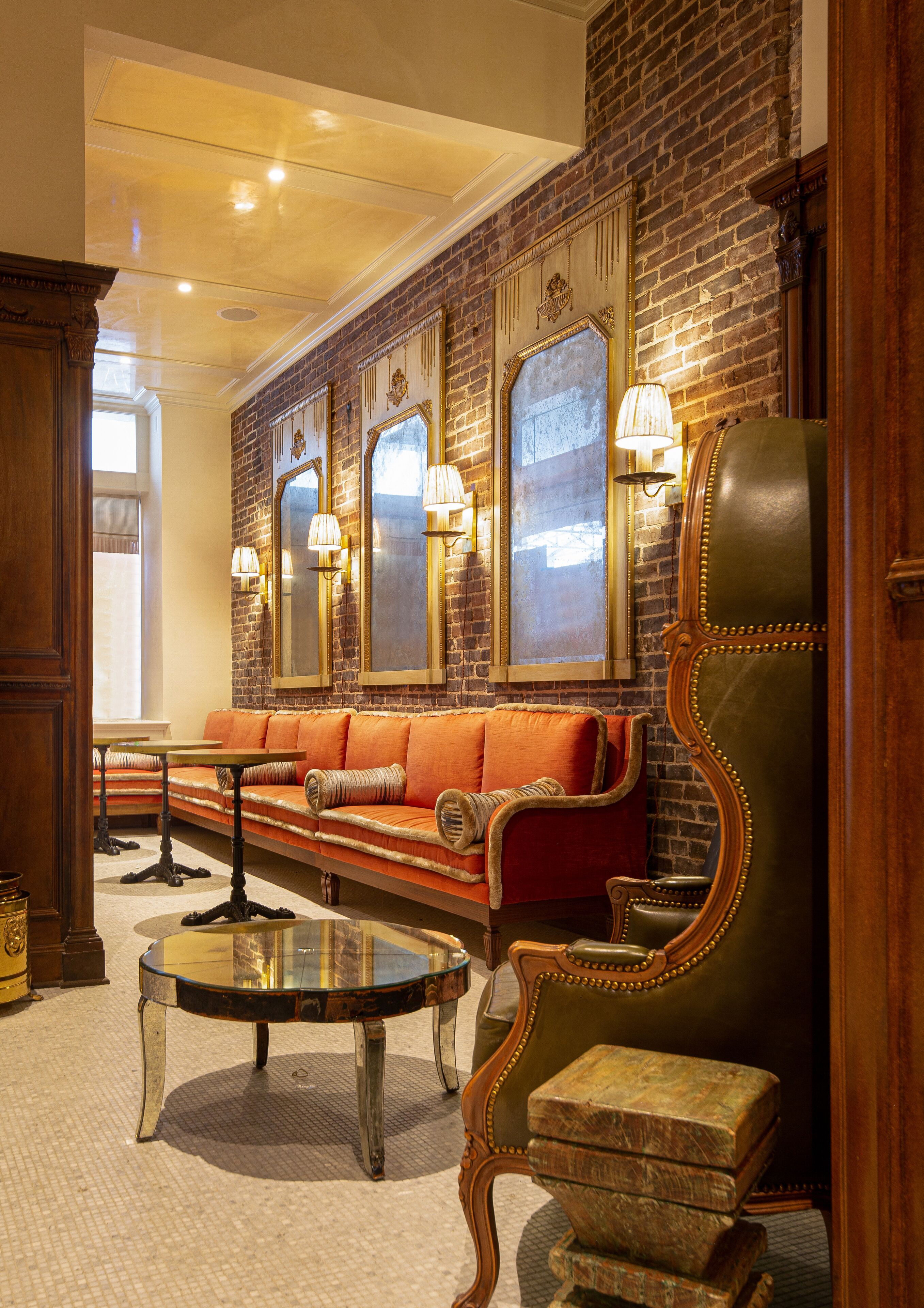 A lobby with a brick wall, leather seating, a round glass table, and wall-mounted lamps.