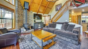 A cozy living room with a stone wall, a fireplace, a wooden ceiling, and a staircase leading to another level.