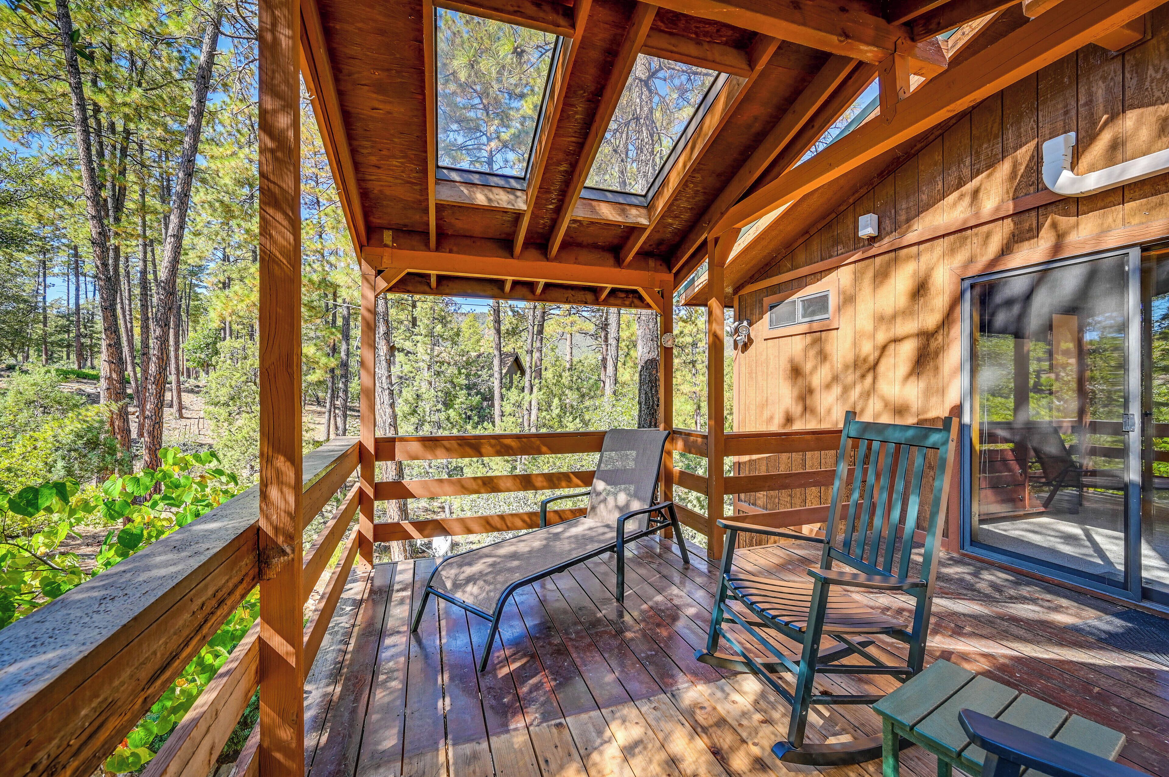 Une terrasse en bois avec un banc et un fauteuil à bascule, donnant sur une zone boisée.