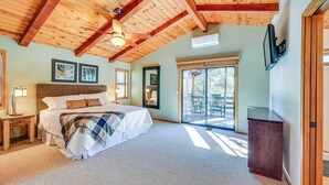 A bedroom with a large bed, wooden ceiling beams, a ceiling fan, and a sliding glass door leading to a balcony.