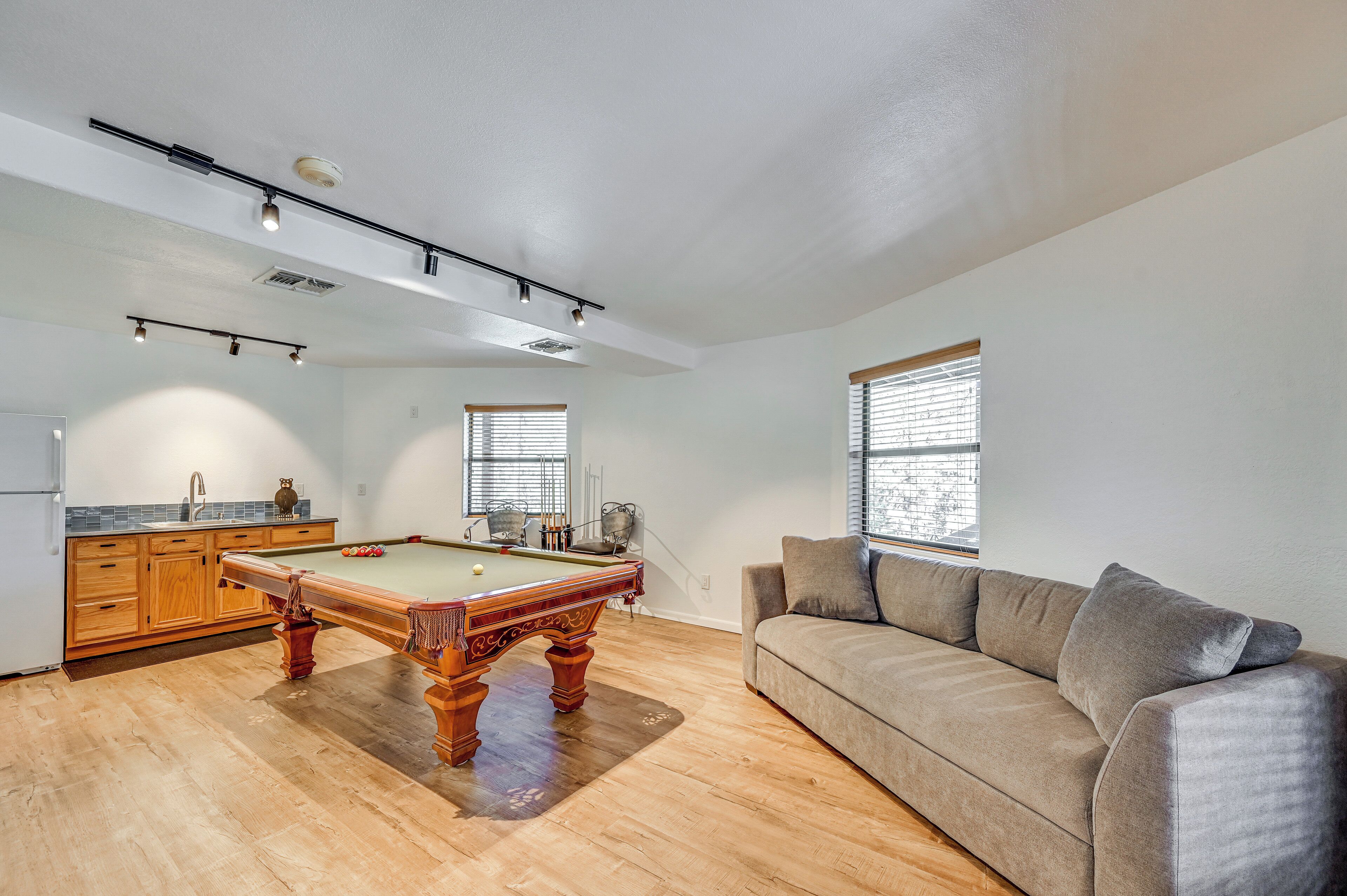 A spacious living area with a pool table, a sofa, and a kitchen with wooden cabinets.