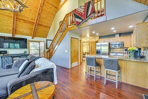 A spacious living area with a wooden ceiling, a staircase, a kitchen with modern appliances, and a cozy seating area.