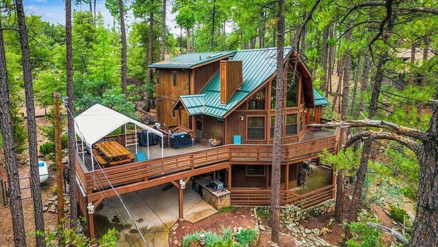 A cabin with a deck, a covered outdoor seating area, and a stone foundation.