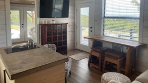 A kitchen with a large island, wooden cabinets, a television, and a dining area with stools. - AMAZING Cabin in the Heart of the Hill Country w/ breathtaking views,Pool & Spa! (Dripping Springs)