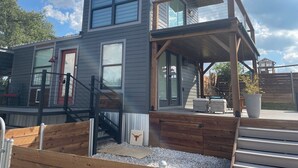 A modern two-story house with a covered porch, a staircase, and a small deck area. - AMAZING Cabin in the Heart of the Hill Country w/ breathtaking views,Pool & Spa! (Dripping Springs)