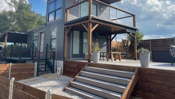 A modern two-story house with a covered patio, wooden deck, and a staircase leading to the upper level. - AMAZING Cabin in the Heart of the Hill Country w/ breathtaking views,Pool & Spa! (Dripping Springs)