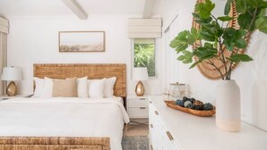 A bedroom with a wooden headboard, white bedding, a bedside table with a lamp, a decorative mirror, and a plant on a dresser. - Gigi's Luxury Beach Hideaway- 3 BDRM- Cowpet Bay West- East End- Pool & Beach
 (St Thomas)