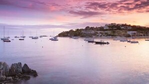 A coastal scene with boats anchored near a rocky shore and a settlement in the background. - Gigi's Luxury Beach Hideaway- 3 BDRM- Cowpet Bay West- East End- Pool & Beach
 (St Thomas)