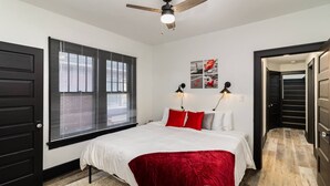 A bedroom with a bed, a ceiling fan, a window with blinds, a door, and a hallway. - Sand & Sun Getaway | Drive to Beach Game Room + 2 Living Areas |Game Room | Minutes to Beach (Michigan City)