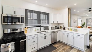 A modern kitchen with white cabinets, stainless steel appliances, and a large window with blinds. - Sand & Sun Getaway | Drive to Beach Game Room + 2 Living Areas |Game Room | Minutes to Beach (Michigan City)