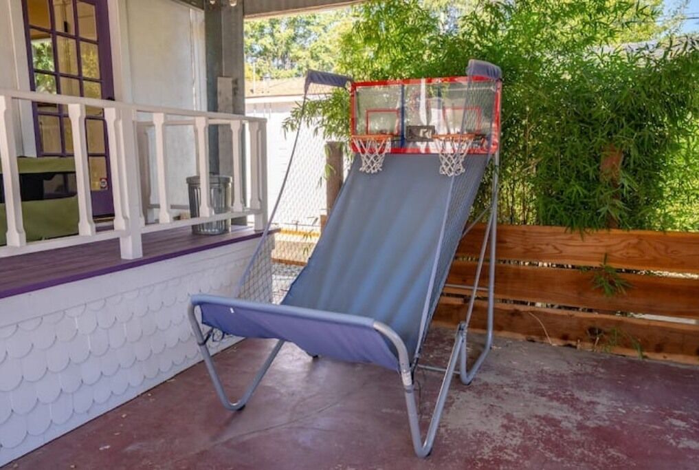 Un espace extérieur abrité comprenant un fauteuil de jardin bleu, un panier de basketball et une clôture en bois.