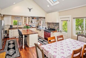 A spacious kitchen with a central island, wooden cabinets, and a dining area with a floral tablecloth.