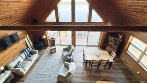 Een ruime loft met hoge plafonds, houten wanden, een gezellige zithoek met banken en een salontafel, een eettafel met stoelen, en grote ramen met uitzicht op de omgeving.