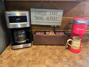 A coffee maker, a sign with coffee, lake, wine, and repeat, a mug, and a coffee pod box.