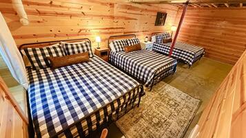 A cozy cabin-style room with three beds, each with checkered bedding, a wooden floor, and a rug.