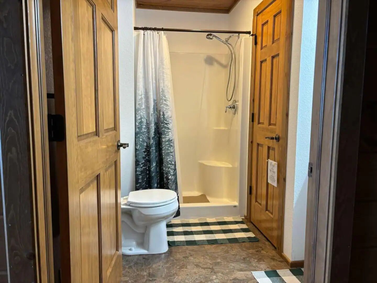 A bathroom with a toilet, shower, and checkered floor mat.