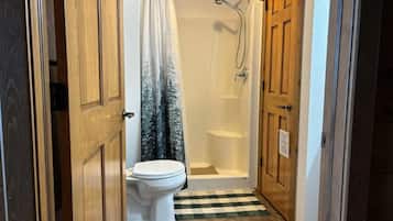 A bathroom with a toilet, shower, and checkered floor mat.