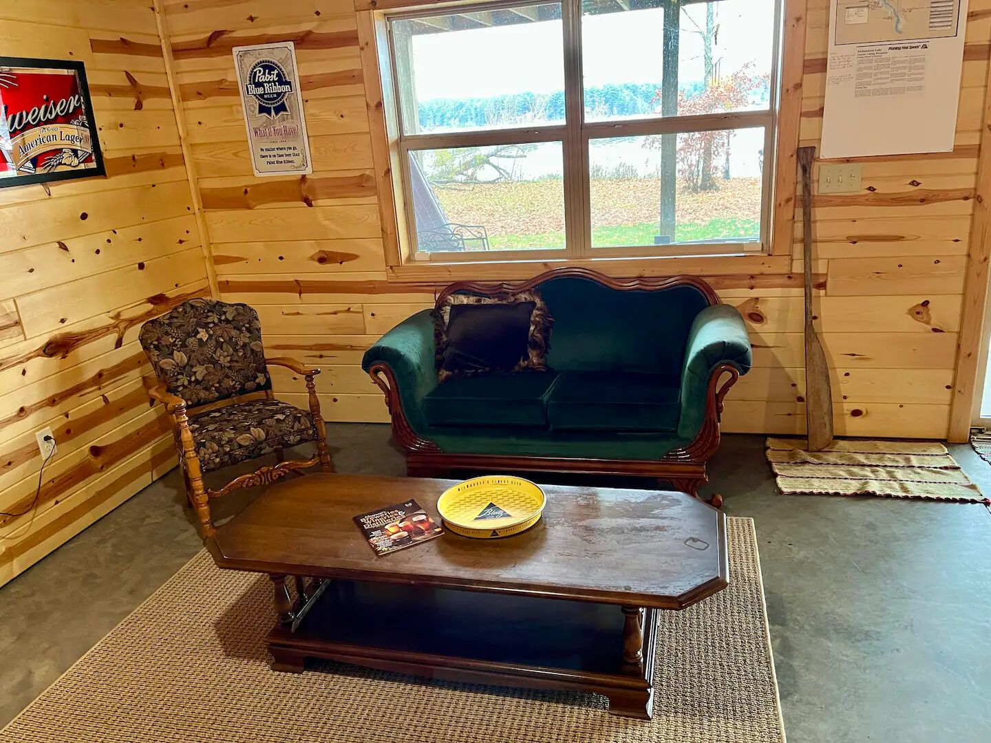 A wooden cabin interior with a green sofa, a floral armchair, and a wooden coffee table.
