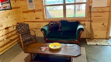 A wooden cabin interior with a green sofa, a floral armchair, and a wooden coffee table.