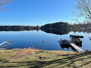 A calm lake with a dock, a boat, and a grassy area with a lamppost.