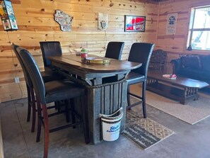 A wooden interior with a round table, four chairs, a bucket labeled "Blain's Farm & Fleet," and various wall decorations including license plates and a Budweiser sign.
