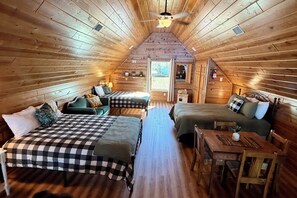 Quarto de sótão aconchegante com duas camas, uma mesa pequena e um ventilador de teto.