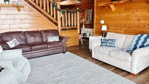 Een houten cabin interieur met een bruine leren bank, een witte bank en een grijze vloerkleed.