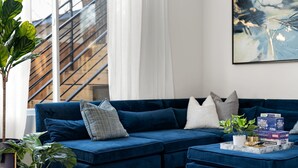 Uma sala de estar moderna com um sofá seccional azul, uma mesa de centro e uma planta grande.