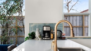 Cozinha moderna com bancada branca, cafeteira, garrafa de azeite e uma escultura branca decorativa.