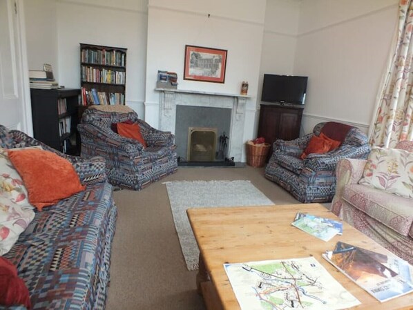 Ein Wohnzimmer mit gemusterten Sofas, einem Kamin, einem Bücherregal und einem Fernseher.