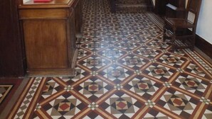 Ein Korridor mit einem gemusterten Boden, einem Holztisch, einer Treppe und einem Kronleuchter.
