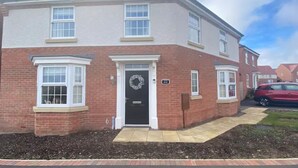 A two-story residential building with a brick facade, white-framed windows, and a black front door with a wreath. - Comfortable 5-Guest Abode -  in Quiet Village (Grantham)