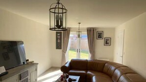 A living room with a leather sofa, a TV on a cabinet, and a hanging light fixture. - Comfortable 5-Guest Abode -  in Quiet Village (Grantham)
