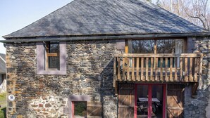 A stone building with a sloped roof, a wooden balcony, and a red door.